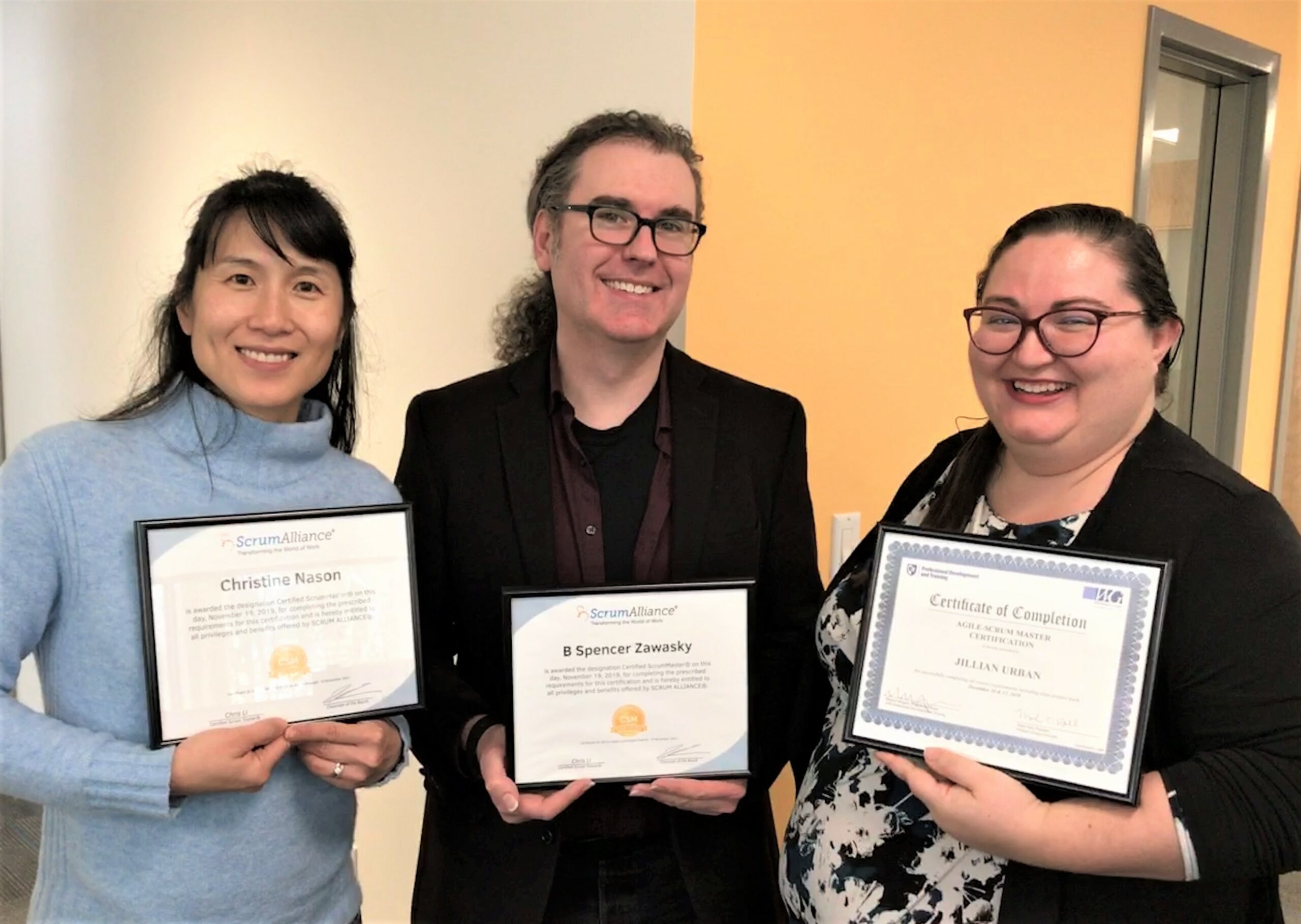 Two females and one male holding scrum master certificates